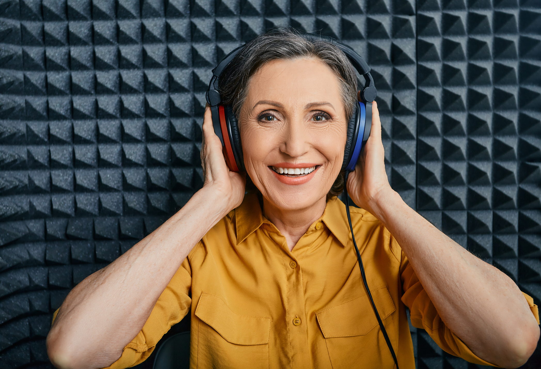 Hearing loss treatment. Positive mature woman wearing audiometry headphones while hearing test and audiogram in special audio room Hearing loss treatment. Positive mature woman wearing audiometry headphones while hearing test and audiogram in special audio room